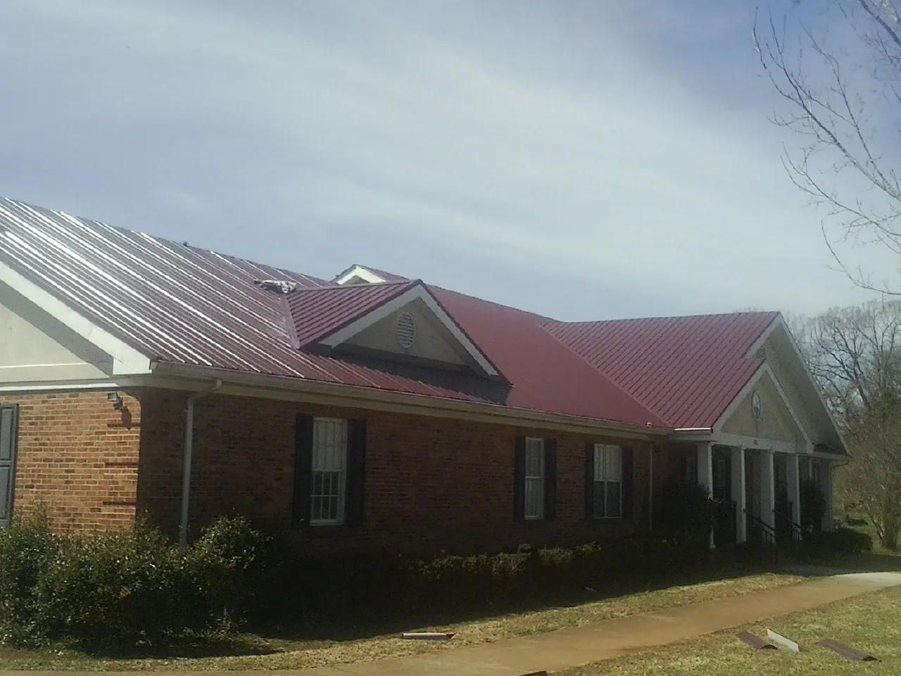 Red metal roof with gabled entries on a long brick building, from a Hail Damage Roof Repair job in Rexburg