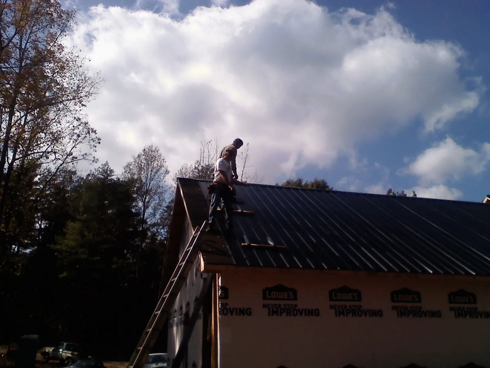 Roofer fastening dark metal panels high against a cloudy sky, from a Roof Inspection job in Rexburg