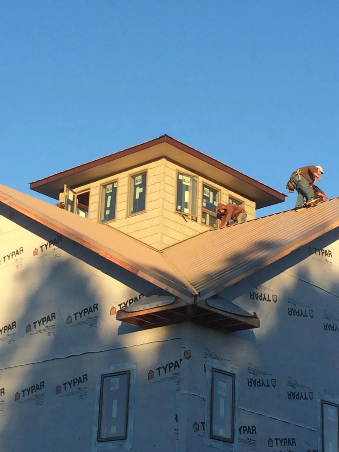 Roofers working around a rooftop cupola on a new metal roof at sunset — Roof Waterproofing in Rexburg by Roofing Brothers